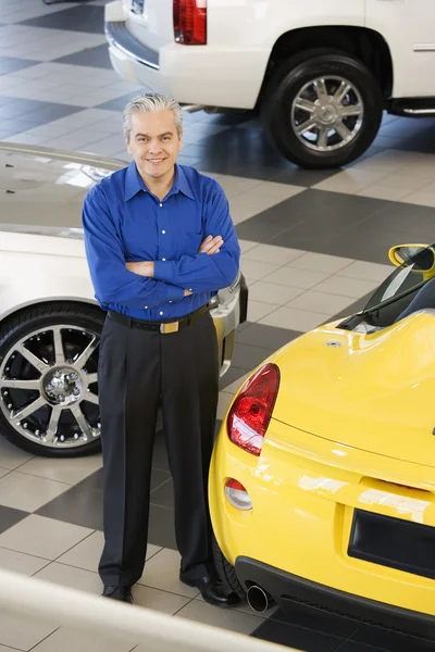 Hispanic car salesman next to new cars