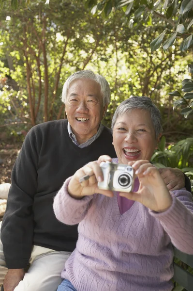 Senior Asian couple sitting on a park bench with a digital camera
