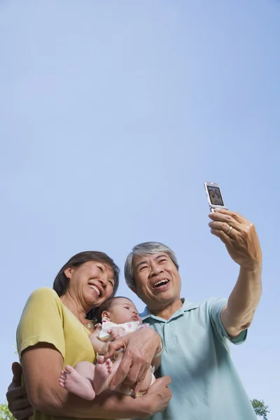 Asian grandparents holding baby grandchild and taking photograph