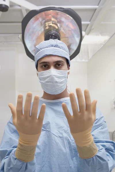 Indian male surgeon holding up gloved hands in operating room