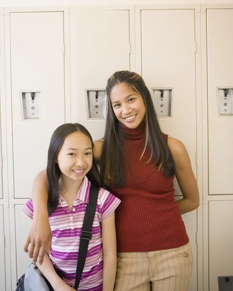 Female teacher with arm around Asian girl in front of school lockers