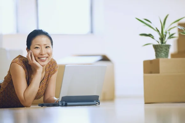 Asian woman using laptop in new house with boxes