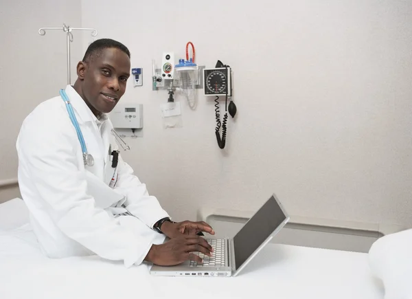 African male doctor using laptop on hospital bed