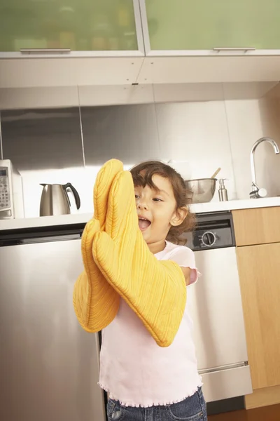 Young girl wearing oven mitts