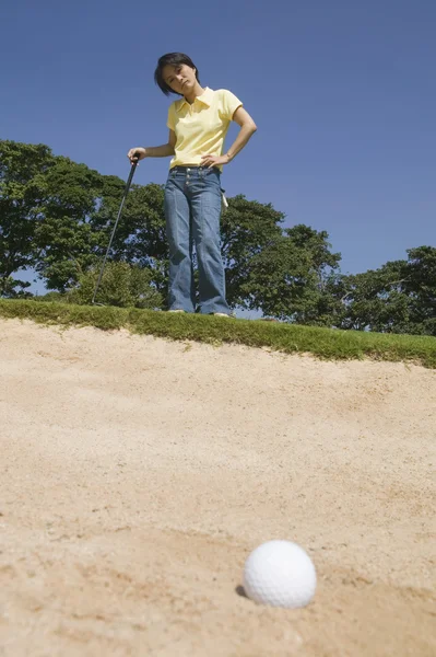 Asian woman looking at golf ball in sand trap