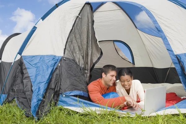 Hispanic couple looking at laptop in tent