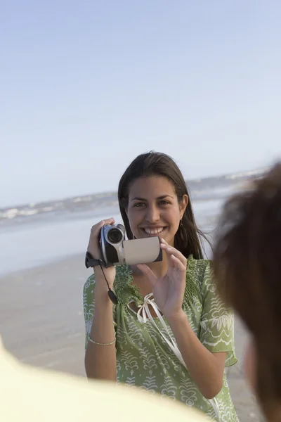 Hispanic girl video recording people at beach