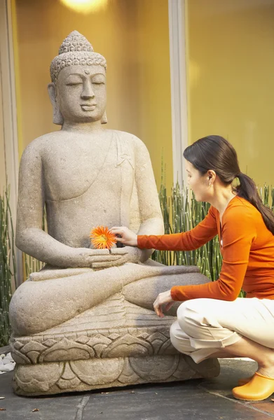 Asian woman placing flower on Buddha statue