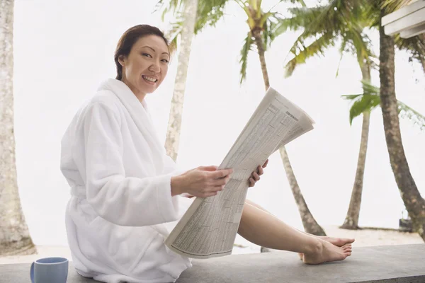 Asian woman in bathrobe reading newspaper