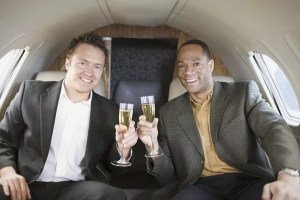 Multi-ethnic businessmen toasting on airplane