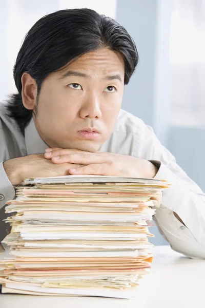 Asian businessman leaning on stack of paperwork