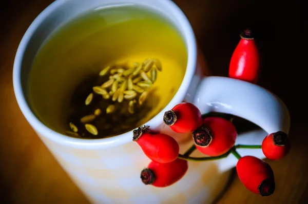 Cup of fennel tea with seeds with rosehip and chestnut decoration. Shaded angles. Selective focus on the rosehips.