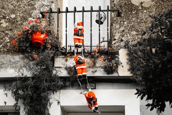 Three Santa Claus figures climbing up a wall into a window. Traditional Christmas decoration. Aged photo.