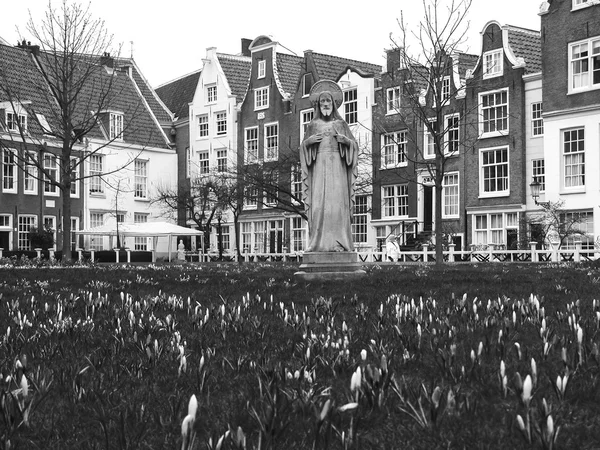 Jesus statue surrounded by violet and white crocus flowers and historic houses in Begijnhof courtyard. (Amsterdam, Netherlands) Aged photo. Black and white.