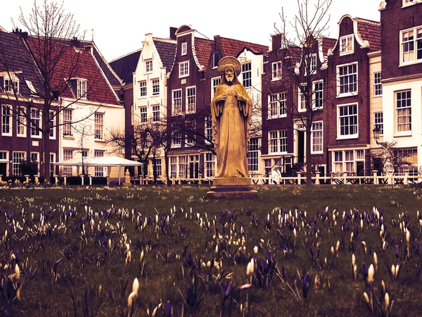 Jesus statue surrounded by violet and white crocus flowers and historic houses in Begijnhof courtyard. (Amsterdam, Netherlands) Toned photo.