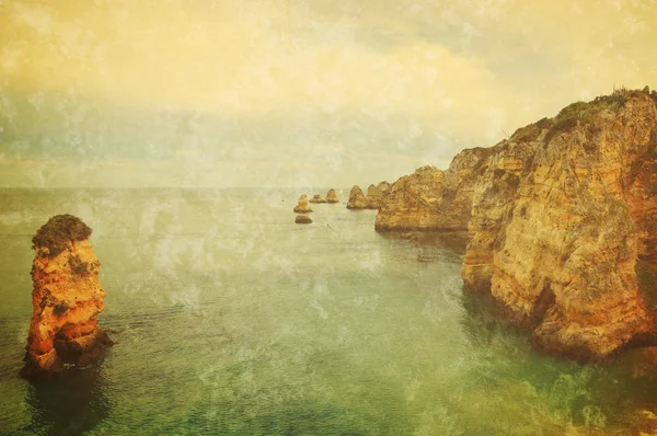 Beautiful rock formations, stone arches and caves at Dona Ana Beach and sailing boats on horizon (Lagos, Algarve coast, Portugal) in the evening light. Retro aged sepia photo with scratches.