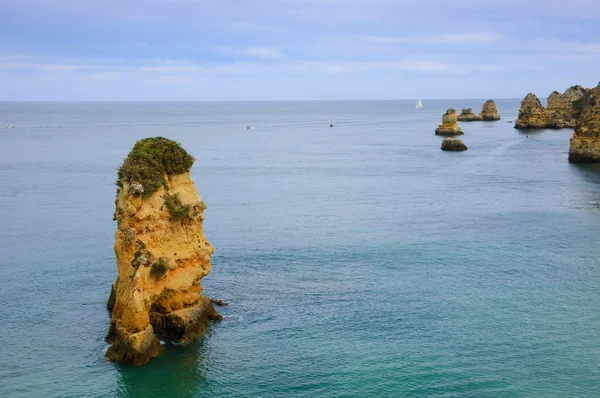 Beautiful rock formations, stone arches and caves at Dona Ana Beach and sailing boats on horizon (Lagos, Algarve coast, Portugal) in the evening light.