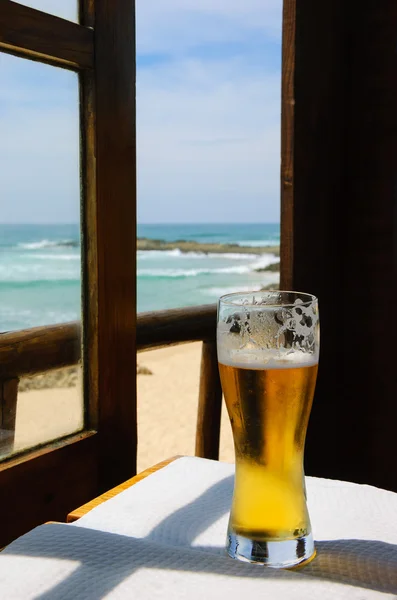 Cold beer on cafe terrace with the view on the ocean beach through the opened window. Algarve, Portugal. A game of light an shadow.