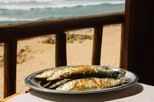 Traditional Portuguese dish -  grilled sardines - served at restaurant terrace with ocean beach view. Algarve, Portugal.