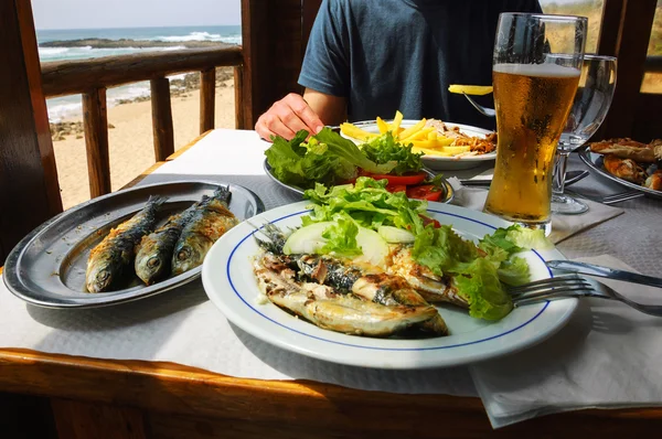 Traditional Portuguese lunch -  grilled sardines and chicken - at restaurant terrace with ocean beach view. Algarve, Portugal.