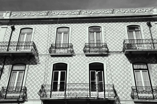 Typical old building in the centre of Lisbon (Portugal). Colorful  ceramic tiles (azulejos) with floral pattern, balconies and roof border with male faces.  Aged photo. Black and white.