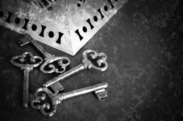 Jewelry box and four vintage keys. Retro aged toned photo with scratches. Black and white.