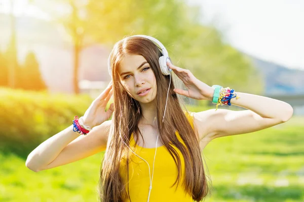 Young woman listening to music on headphones outdoors in park