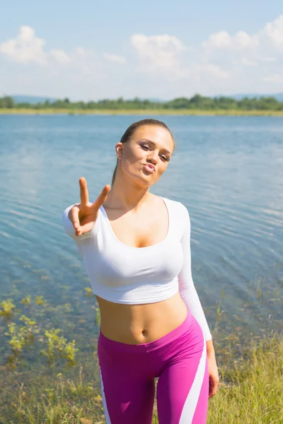 Young fitness woman gesturing peace and making kissy face outdoors by the lake