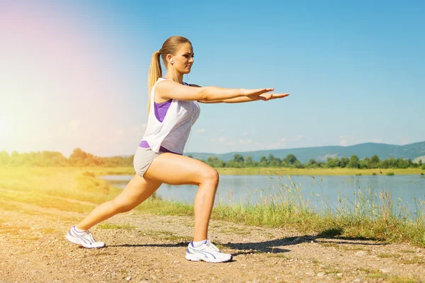 Young woman training doing squats outdoors on sunny summer day