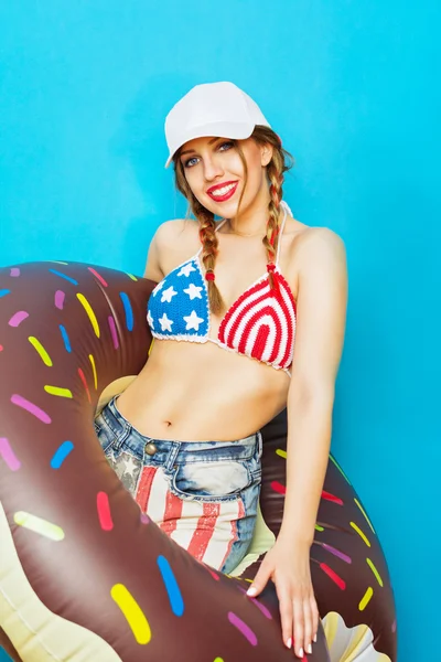 Cool young woman in American flag bikini with inflatable donut float