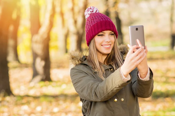 Beautiful young woman in jacket and knitted hat taking a selfie in autumn on smart phone