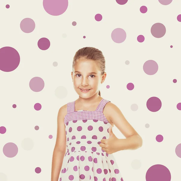 Cute little girl in dress with purple dots gesturing thumbs up