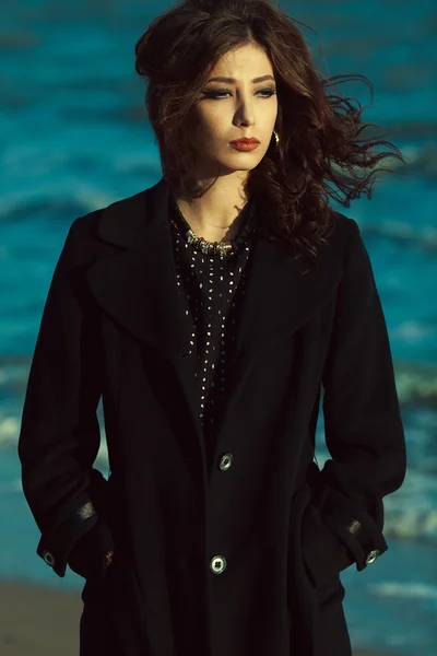 Bella donna concept. Beautiful brunette with long curly hair in black coat