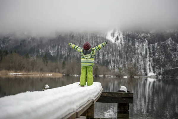 Toddler standing at the end of a snow covered pier on a lake