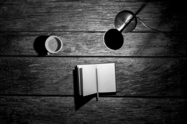 Lit desk lamp, open notebook with pencil and cup of coffee on a