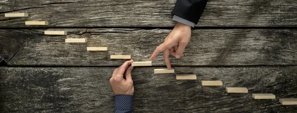 Hand of a businessman supporting a wooden step for his colleague