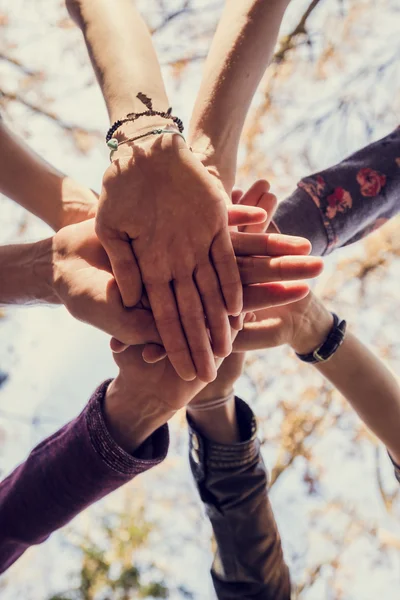 View from below of eight hands making a pile outside in nature