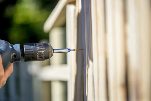 Person building a wooden fence with a drill and screw