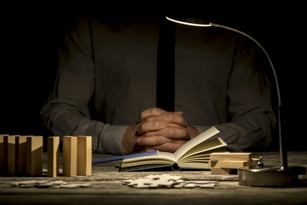 Folded hands near book and puzzle pieces