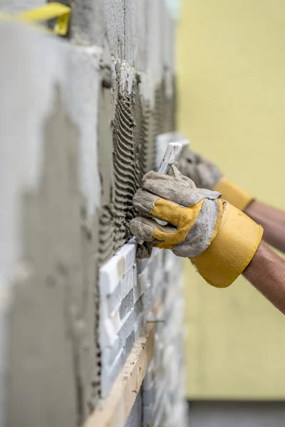 Hands of worker installing ceramic wall tiles