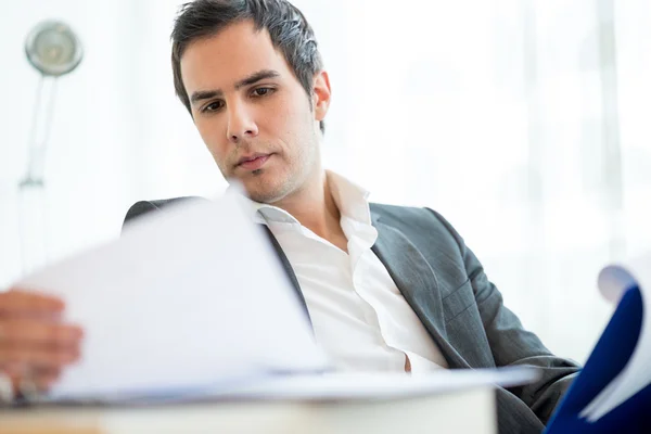 Successful young executive in a jacket sitting reading a report or document