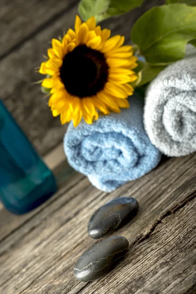 Spa setting with a towels, sunflower on top, massage stones, and