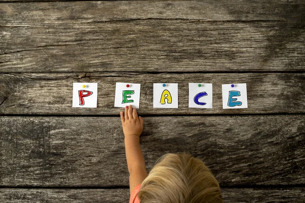 Top view of toddler girl touching the word Peace pinned on a tex