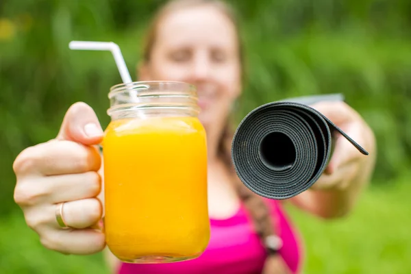Fitness woman with yoga mat holding a glass of orange juice