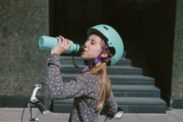 Teenage girl resting in a street with a bicycle drinking water