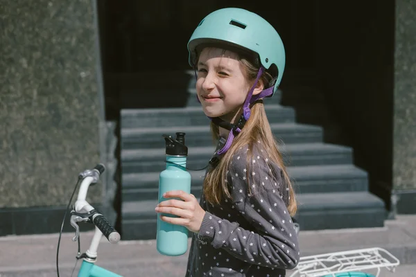 Teenage girl resting in a street with a bicycle drinking water