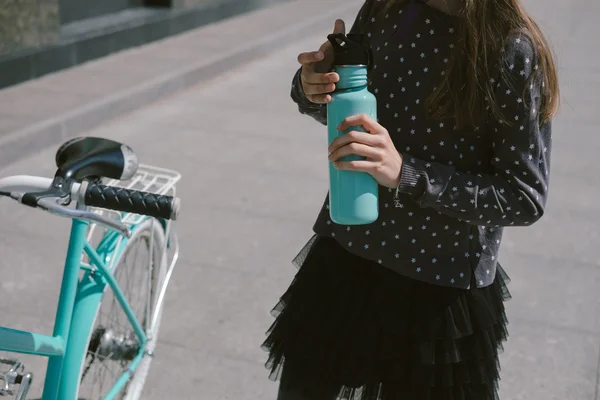 Teenage girl resting in a street with a bicycle drinking water