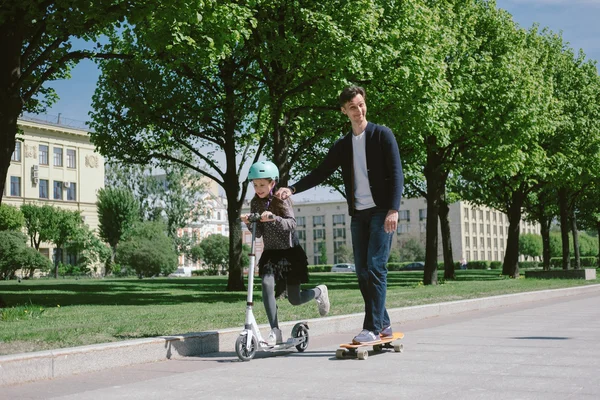 Dad and daughter ride a scooter and skate together