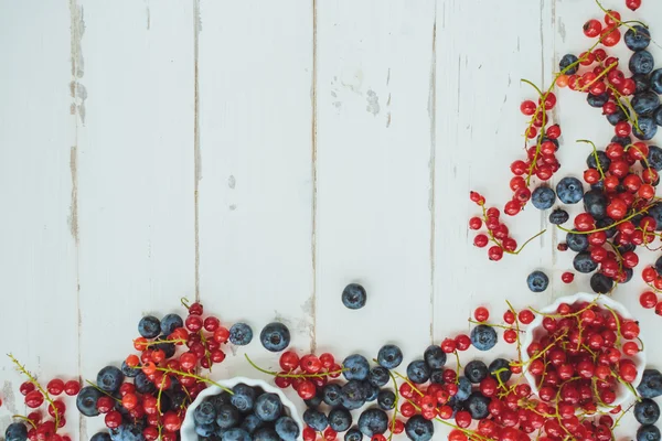 Red currants , blueberries  on white wooden background, top view