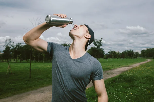 Young exhausted athlete drinking  fresh water to refresh during